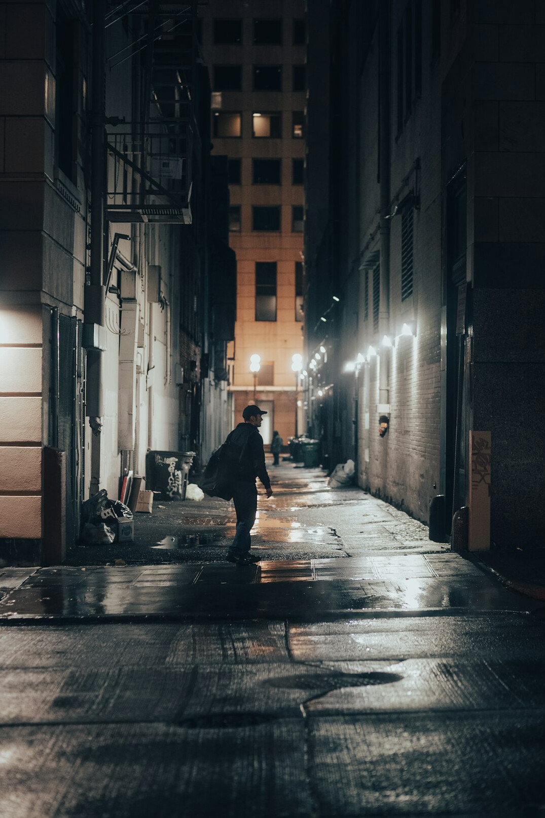 Rainy city street at night with a lone silhouette under a streetlight